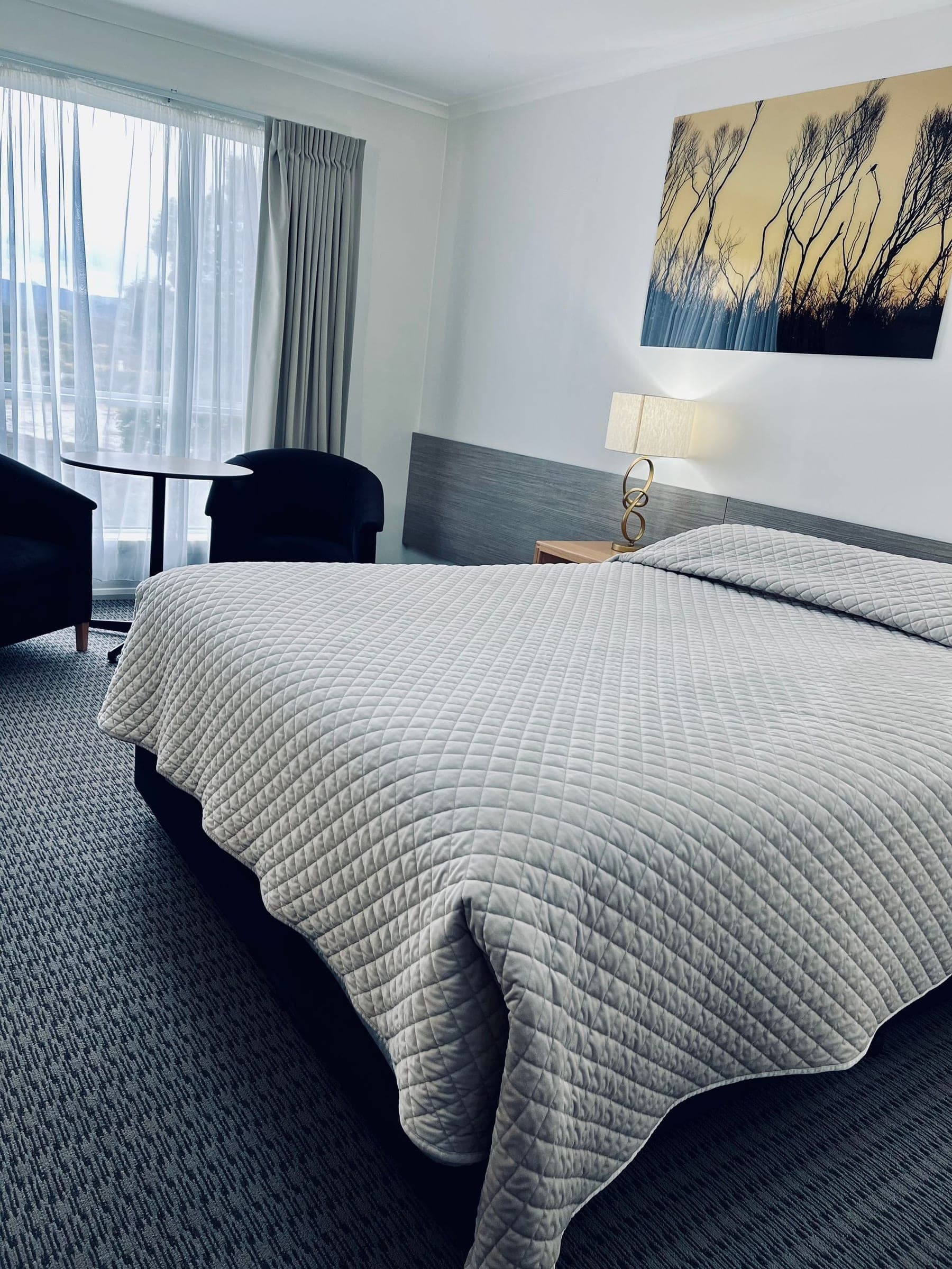 Queen guest room with armchairs and a window at the Heemskirk Motor Hotel